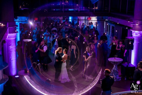 Purple Light Isolates Couple Under High Angle During Alexandria First Dance Torpedo Factory, Old Town Alexandria, VA, Reception Venue — During their first dance, the couple invite all wedding guests to join them, while a high-angle shot, creative in-camera effect, and dramatic backlight isolate them under purple lighting ambiance