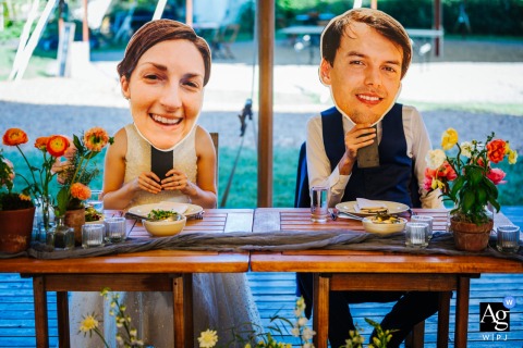 Blooming Hill Farm, New York — The couple poses at their wedding holding giant marathon face cutouts on sticks over their faces, adding a playful and artistic element to the celebration.