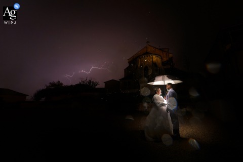 Wedding Couple Illuminated Under An Umbrella Against A Dark Stormy Sky At A Dordogne Reception Location Creates A Dramatic Portrait Wedding couple illuminated under an umbrella against a dark, stormy sky at a Dordogne reception venue.