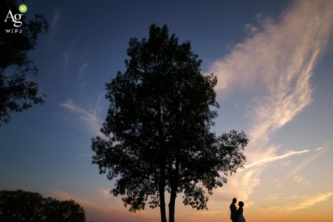 Silhouetted Couple Stands at Sunset in Dordogne France Using Natural Light at Reception Venue A couple’s silhouette is set against the sunset at a reception venue in Dordogne, France, using natural lighting to create a defined outline of the newlyweds.