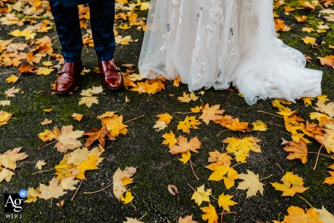 Outside The Pumping House Wedding Venue In Nottinghamshire, UK, The Couple’s Shoes Are Framed By Autumn Leaves In A Detail Shot Outside the Pumping House wedding venue in Nottinghamshire, UK, the bride and groom’s feet are shown in a detail shot, shoes framed by a path strewn with yellow autumn leaves.