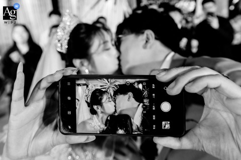 In Kaifeng, Henan, The Couple Shares A Kiss While Snapping A Selfie, Blending Modern Romance And Tradition For Their Portrait In Kaifeng, Henan, the bride and groom share a kiss while snapping a selfie, blending modern romance with tradition in their celebratory portrait.