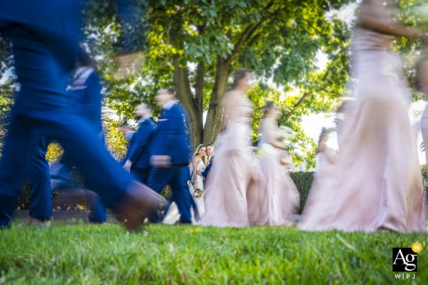 In Cleveland Museum Of Art, Ohio, The Couple Peeks Out Playfully From Between Their Blurred Wedding Party For An Artful Motion Portrait In Cleveland Museum of Art, Ohio, the bride and groom cleverly peek out from between the blur of their wedding party, blending playfulness with fine art surroundings.