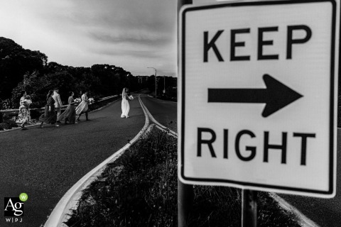 Bridal Party Crosses Road at Keep Right Arrow Sign on Provincetown Beach in Massachusetts For Candid Portrait On Provincetown Beach in Massachusetts, the bridal party crosses the road beneath a bold painted arrow, highlighting the contrast between the structured street sign and their spontaneous procession.
