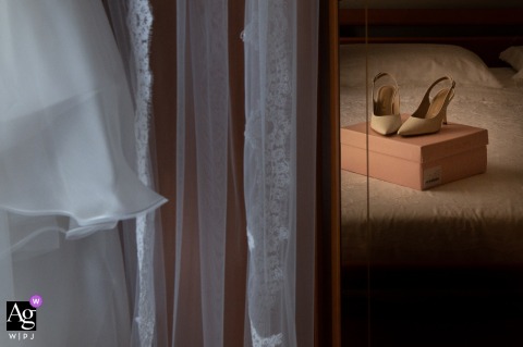 At The Bride’s Home In Gonzaga, Mantua, Italy, Warm And Cool Lights Showcase Detailed Texture Of Gown, Veil, And Shoes At the bride’s home in Gonzaga, Mantua, Italy, warm and cool lights blend to showcase detailed textures of the gown, veil, and wedding shoes.