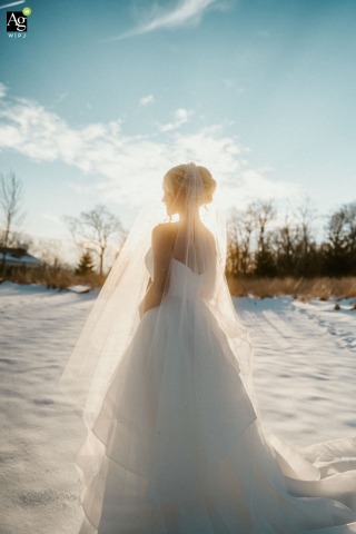 Bride Outdoors in Snowy Landscape at Overlook Barn in North Carolina With Sunlit Features At Overlook Barn in North Carolina, the sun is visible behind the bride, its light highlighting her features as she stands outdoors in the white snowy scene.