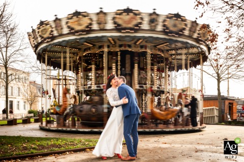 Couple Stands in Front of Carousel for Portrait in La Rochelle Charente Maritime France In La Rochelle, Charente Maritime, France, the couple stands together in front of a carousel, the background adding a sense of place as they pose for a fun portrait.