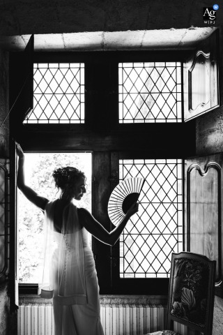 At Château Sainte Foy d'Anthe In France, The Bride Is Captured Facing A Window In A Serene Preparation Portrait At Château Sainte Foy d'Anthe in Lot-et-Garonne, France, the bride is captured in a serene portrait facing the window at the end of her preparations.