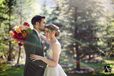 Newlyweds Stand at River Bend in Lyons Colorado With Rainbow Lens Flare Streaming In At River Bend in Lyons, Colorado, the newlyweds stand together in the afternoon, a rainbow lens flare from the sun streaming into the frame as they share a quiet exchange.