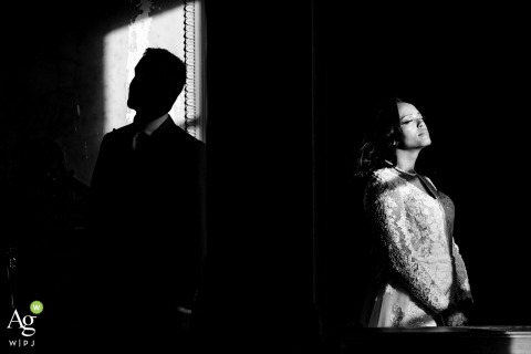 Minimalistic Silhouette and Profile Portrait Places Couple Against Dramatic Backdrop at Chateau de Beaujeu A couple stands, him in silhouette at Chateau de Beaujeu, their forms visible against a lit backdrop, producing a minimalistic and dramatic wedding portrait.