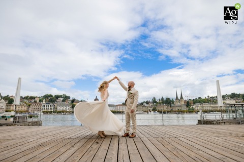 Bride Twirls on Boardwalk With Groom Creating Waterside Motion in Lucerne Switzerland On the boardwalk at the water of Lucerne, Switzerland, the groom twirls the bride, creating movement and a dynamic composition within the urban setting.