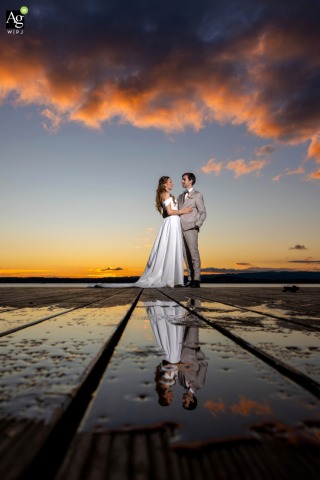 Sunset Colors Reflect Across Water as Couple Poses Beside Lake of Zoug Switzerland On the shores of Lake of Zoug, Switzerland, sunset colors are reflected across the water as the environment and couple intersect in the frame.