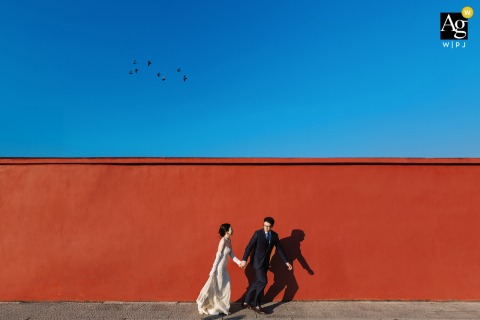 In The Park In Nanping, Fujian, The Bride And Groom Run Along A Red Brick Wall With Vibrant and Bold Backdrop In the park, the bride and groom run together along a red brick wall in Nanping, Fujian, the vibrant backdrop adding energy to their wedding photo.