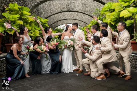   Zephyr Palace at Villa Caletas Hotel in Jaco, Costa Rica, is the scene as the bride and groom share a kiss while their wedding party celebrates around them.