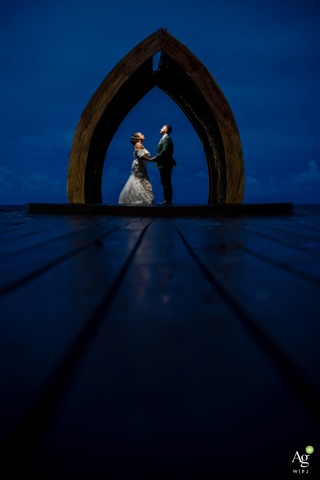 Distinctive Architecture and Blue Hour Lighting Emphasize Couple’s Portrait Session in Cancun Mexico During blue hour in Cancun, a couple is photographed with flash against distinctive architecture, with the lighting conditions emphasizing the background and structural elements around them.