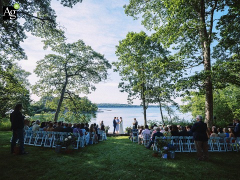 Loving Vows Exchanged Under Shaded Trees Beside the Water at The Harpswell Inn in Maine The ceremony scene at The Harpswell Inn in Harpswell, Maine, is filled with anticipation and gentle light, guests and couple alike gathered for a loving exchange of vows under the trees in the shade by the water.