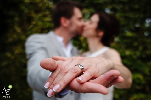 Hands Entwined Showcasing a Wedding Ring While Couple Shares a Blurred and Soft Kiss in Moselle In the foreground, the couple’s hands are entwined to showcase a wedding ring, while a soft, blurred kiss between bride and groom brings a romantic touch to the reception scene in Moselle.