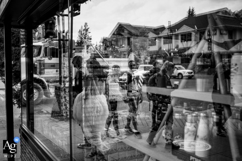 The Couple’s Reflection Appears In A Window On A Busy Banff National Park Street In Banff National Park, the couple’s reflection appears in a window as they walk a busy street, blending the vibrant surroundings.