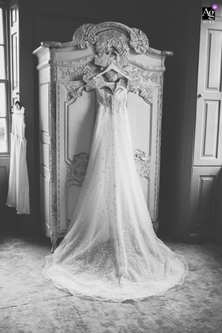 The Wedding Dress Hangs Gracefully At Newton Hall In Northumberland, UK, Its Delicate Fabrics Catching The Light At Newton Hall in Northumberland, UK, the wedding dress hangs gracefully, its delicate fabrics catching the light and hinting at the anticipation of the day.