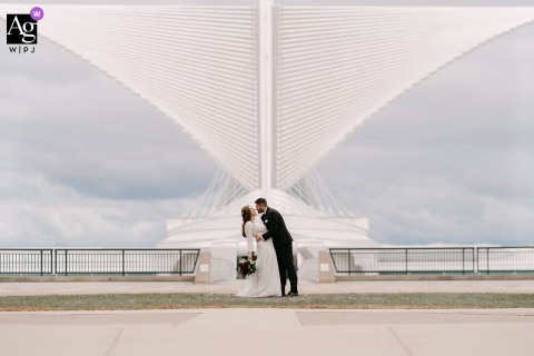 Kissing In Front Of Architectural Wings At Milwaukee Art Museum, The Couple’s Connection Is Highlighted By The Striking Background At the Milwaukee Art Museum in Wisconsin, the couple kisses in front of the museum’s dramatic architectural wings, the striking background highlighting their connection.