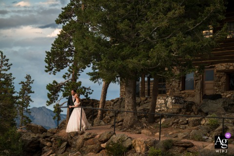 Portrait Of The Couple In Front Of Historic Mountainside Lodge At YMCA Of The Rockies, Estes Park, With Dramatic Landscape In front of the historic Mountainside Lodge at YMCA of the Rockies, Estes Park, Colorado, the couple poses together with mountain scenery creating a breathtaking wedding portrait.