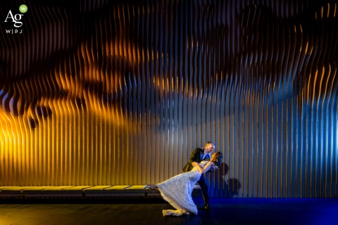 Dramatic Cross Lighting Highlights a Dancing Couple at Blue Credit Union Event Center in Cheyenne Wyoming As the couple dances at Blue Credit Union Event Center in Cheyenne, Wyoming, dramatic orange and blue cross lighting transforms the wooden wall into a vivid backdrop that highlights their connection and movement.