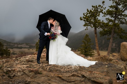 As Rain Falls In Rocky Mountain National Park, Colorado, The Couple’s Portrait Embraces Natural Setting And Adventurous Spirit As rain begins to fall in Rocky Mountain National Park, Estes Park, Colorado, the couple stands outside, the natural setting and weather making their portrait adventurous and memorable.