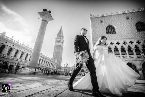 Low-Angle Photograph In St. Mark’s Square, Venice Shows Newlyweds Walking Hand In Hand Amid Graceful Venetian Architecture A low-angle photo in St. Mark’s Square, Venice, shows the newlyweds walking hand in hand, the famous Venetian architecture rising gracefully around them.