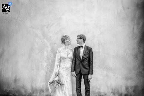 In Thiene, Vicenza, The Couple Poses In A Minimalist Black And White Portrait Against A Modern, Unadorned Venue Wall At Thiene in Vicenza, Italy, the couple stands together in a minimalist black-and-white portrait, their figures outlined against a bare, unadorned wall for a modern, understated look.
