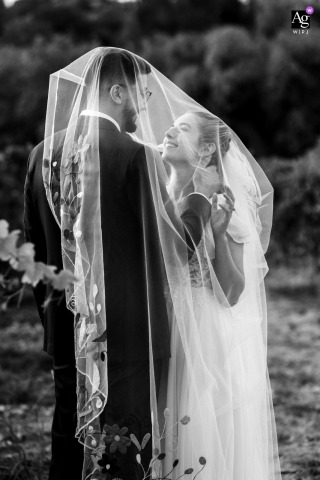 Among Vineyard Rows At The Isere Reception Site, The Couple Stands Beneath A Delicate Veil In Romantic Style Beneath a delicate veil, the couple stands among Isere vineyard rows at the reception site, the vineyard landscape adding romance and intimacy to their portrait.