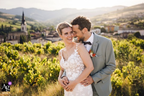 Newlyweds Laugh And Embrace At Sunset Above The Village, The Landscape Spreading Warmth Throughout Their Portrait At the reception venue above the village, the newlyweds embrace and share laughter during sunset, the soft glow and sweeping landscape adding warmth to this joyful wedding portrait.