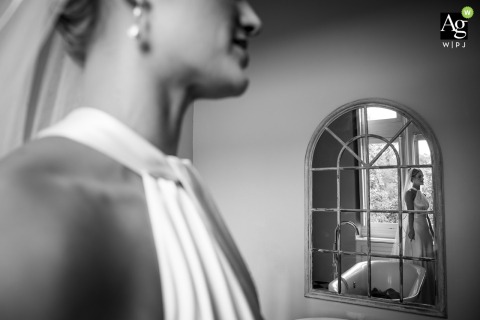 Bride Stands Near Window, Reflection Framed At Chateau De Lisse Réaup-Lisse France At Chateau de Lisse, Réaup-Lisse in Lot et Garonne, France, the bride quietly stands near the window, her reflection delicately framed in an arched mirror just before her ceremony.