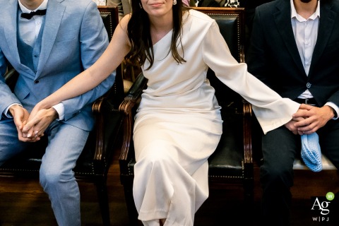 Bride Holds Husband And Brother’s Hands At City Hall Pau Pyrénées France During a civil ceremony at the city hall of Pau in the Pyrénées, the bride warmly holds the hands of her husband and brother, symbolizing the bonds of love and family.