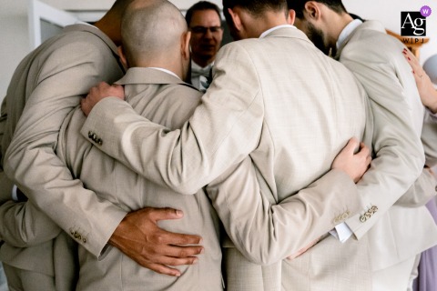 The Groom In Pau, Pyrénées-Atlantiques, Stands Arm In Arm With Men For Group Prayer Before The Ceremony Begins. At the same Pau venue, the groom stands arm in arm with friends and family, heads bowed in a group prayer before the ceremony begins, the setting emphasizing togetherness.