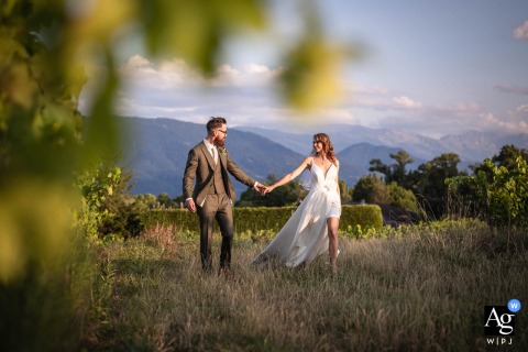 Newlyweds Walk Between Vineyard Rows At Clos De Florie, Savoie, France, Peaceful Scenery Framing Their Serene Wedding Portrait The newlyweds are seen walking between rows of vineyards at Clos de Florie in Savoie, France, the lush landscape lending a peaceful, scenic atmosphere to their portrait.