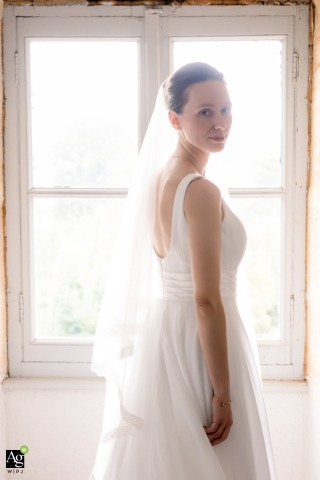Bride Radiates Elegance In Whitewashed Scene And Framed By Historic Windows At Château De Cypierre Saône-et-Loire Poised in her gown at Château de Cypierre in Saône-et-Loire, the bride radiates elegance, framed by the historic window architecture and soft natural light.