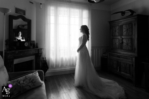 Bride Prepares For Wedding In Softly Lit Room At Domaine Des Oliviers Paris In a softly lit room at Domaine des Oliviers, Paris, the bride prepares for her wedding, her expression and attire reflecting anticipation during the getting ready phase.