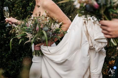   The bride is pictured holding her bouquet and a champagne glass at High Billinghurst Farm Wedding Venue in Surrey, England, blending elegance with the festive spirit of the day.