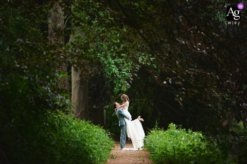  Among the trees of the Amsterdam park, the wedding couple stands together for a composed portrait, the natural environment enveloping them in greenery and soft sunlight.