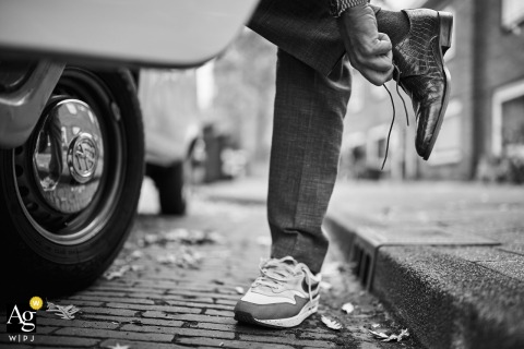 Groom Changes Into Comfortable Shoes On Amsterdam Street Highlighting Practical Detail On the Amsterdam street, a detail shot shows the groom changing into comfortable shoes to drive the van, highlighting a practical and personal aspect of the day.