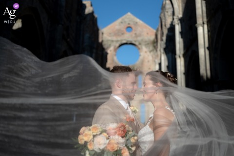Bride’s Veil Flows Elegantly At San Galgano Abbey And Agriturismo Tuscany At San Galgano Abbey and Agriturismo San Galgano in Tuscany, the bride’s veil flows elegantly, adding a sense of depth and sophistication to their portrait within the historic venue.