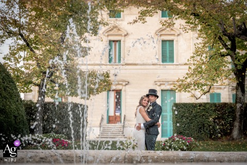 Wedding Couple Posed Behind Magnificent Fountain At Villa Magi Foiano Arezzo Behind the magnificent fountain at Villa Magi, Foiano della Chiana in Arezzo, a composed portrait of the wedding couple is set, with water features adding grandeur to the formal composition.