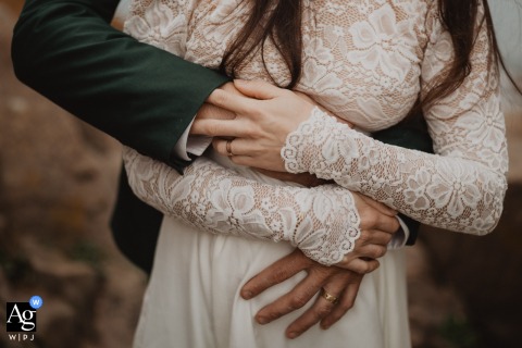 Couple’s Hands Embrace Over Bride’s Pregnant Belly In Morlaix Bretagne France In Morlaix, Bretagne, France, the couple’s hands gently embrace during their photoshoot, one hand resting thoughtfully on the bride’s pregnant belly, in this meaningful wedding detail.