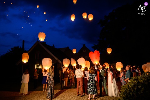 Guests Release Glowing Lanterns As Couple Sends Heart-Shaped Light Skyward At Landgoed Klarenbeek, guests release glowing paper lanterns into the night sky, while the wedding couple send up a heart-shaped lantern, creating a striking scene above the gathered crowd.