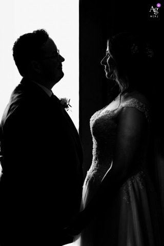Sunlit Doorway At St Giles House Dorset Highlights Bride And Groom Contrast A sunlit doorway at St Giles House in Dorset, UK, creates striking contrast in this scene, highlighting the bride’s white dress and the groom’s dark suit in a visually compelling wedding image.