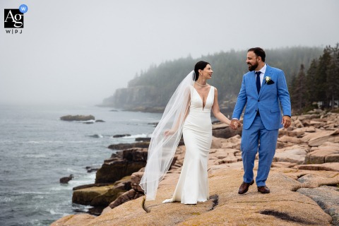   The bride and groom traverse the dramatic cliffs of Acadia National Park in Maine on their wedding day, the sweeping landscape providing a breathtaking backdrop to their walk together.