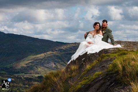  Seated together atop Healy Pass, R574 in Clashduff, Co. Cork, Ireland, the bride and groom take in the expansive mountain views, creating a scene of tranquility and romance.