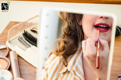 Bride Carefully Applies Lipstick on Wedding Day in Cork, Ireland, Preparing for Celebration with Grace and Anticipation On her wedding day in Cork, Ireland, the bride carefully applies her lipstick in a small mirror, preparing for the celebration with grace and anticipation.