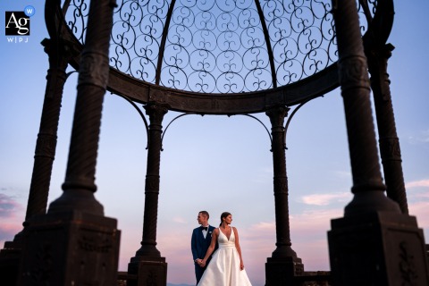 Framed By The Gloriette At Baronesse Tacco In San Floriano Del Collio Framed by the gloriette at Baronesse Tacco in San Floriano del Collio, Gorizia, Italy, the newlyweds pose for a creative sunset portrait against a golden and blue sky.