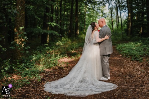 A Tranquil Wedding Portrait Among Tall Trees Near Danzturm In Iserlohn, Germany Amid the woods near Danzturm in Iserlohn, Germany, the newlyweds pose for a portrait among tall trees, the natural setting adding depth and tranquility to their special day.